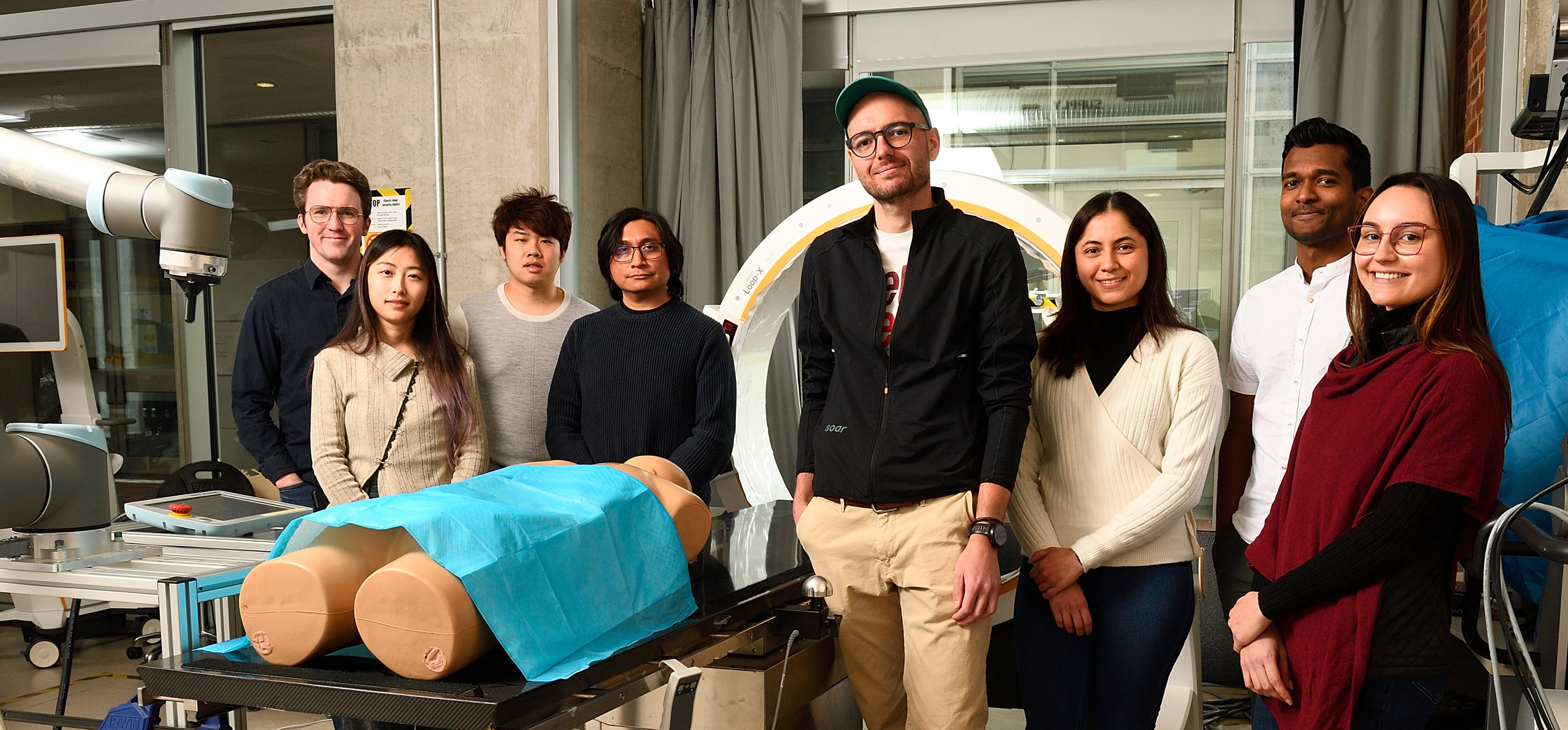 Members of the ARCADE Lab at Johns Hopkins University standing in the research lab alongside a robotic arm and medical imaging equipment